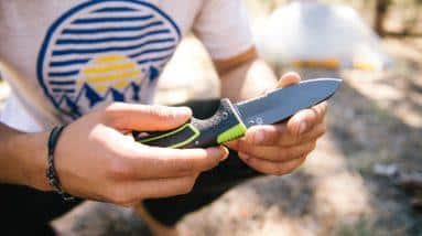 A person honing their survival knife skills in the woods.